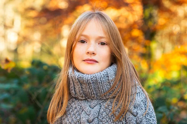 Outdoor portrait of a cute little girl in autumn forest, wearing grey knitted poncho — Stock Photo, Image