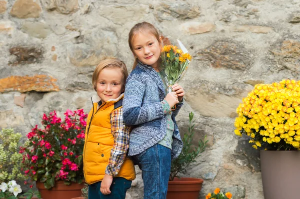 Retrato de outono de duas crianças adoráveis, menina e menino, de pé para trás na frente da parede de pedra com decorações de flores, vestindo jaquetas quentes — Fotografia de Stock