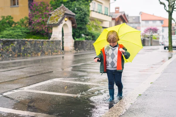 Outdoor portrait of adorable little blond boy with umbrella under the rain, playing in the puddle — Stock Photo, Image