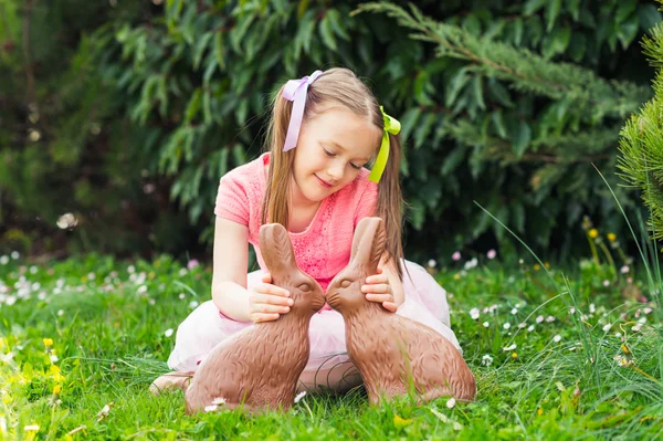 Открытый портрет милой маленькой девочки, играющей в саду с двумя шоколадными кроликами — стоковое фото