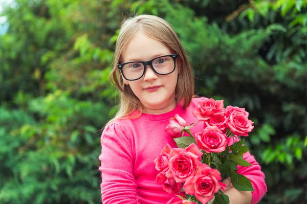Adorable petite fille portant des lunettes, tenant des roses rose vif — Photo