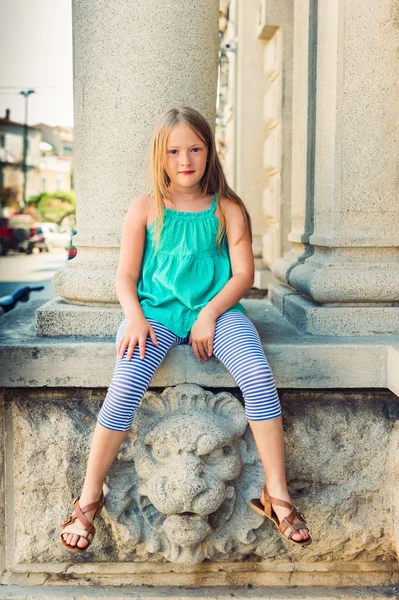 Ritratto estivo di una graziosa bambina che indossa un top verde, sdraiata all'aperto in una città, immagine tonica — Foto Stock