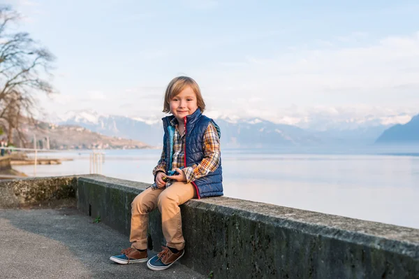 Outdoor portrait of a cute fashion little boy of 4 years old, wearing blue waistcoat, plaid shirt, beige trousers and sneakers — Stock Photo, Image