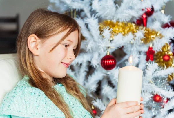 Retrato interior de uma menina bonita na época do Natal, brincando com uma grande vela — Fotografia de Stock