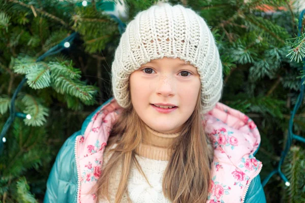 Winter dicht omhoog portret van een schattig klein meisje van 8 jaar oud, naast kerstboom, permanent dragen van een hoed — Stockfoto