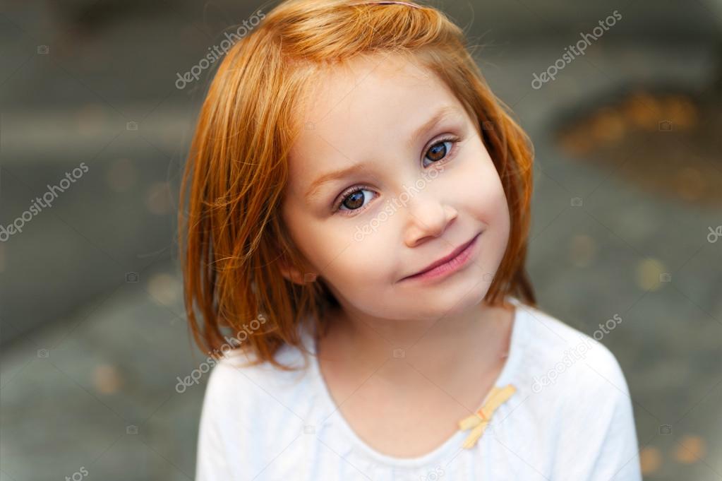 Outdoor close up portrait of cute little girl with red hair