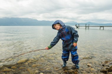 Balık tutma, giyiyor mavi su geçirmez tüm-içinde-bir takım elbise ve yağmur botları gibi davranarak göl kenarında oynayan sevimli küçük çocuk