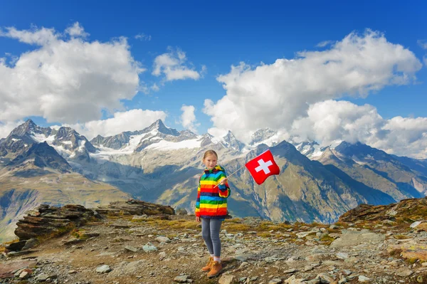 Nettes kleines Mädchen in leuchtend regenbogenfarbenem Mantel, mit Schweizer Fahne vor Gornergrat-Gletscher, Schweiz — Stockfoto