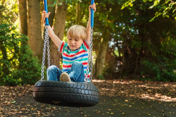 かわいいブロンド少年楽しんで素敵な夏の日にスイングに柄の t シャツを着て — ストック写真