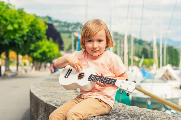 Little happy boy plays his guitar or ukulele — Zdjęcie stockowe