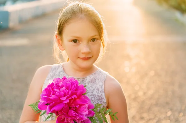 Sunset outdoor portrait of a cute little girl with small bouquet of bright pink peonies — 图库照片