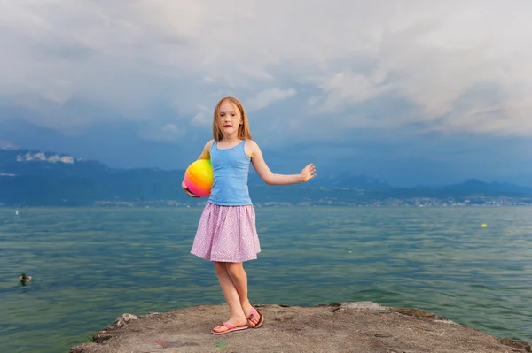Cute little girl resting by the lake at sunset, wearing blue top and pink skirt — Stok fotoğraf