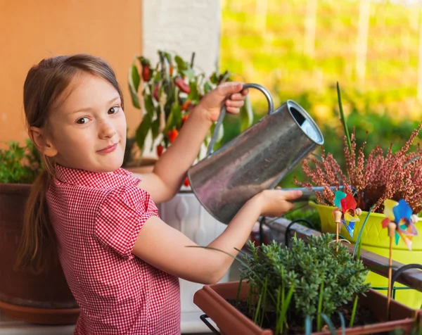 Adorável menina regando plantas na varanda em um dia ensolarado agradável — Fotografia de Stock