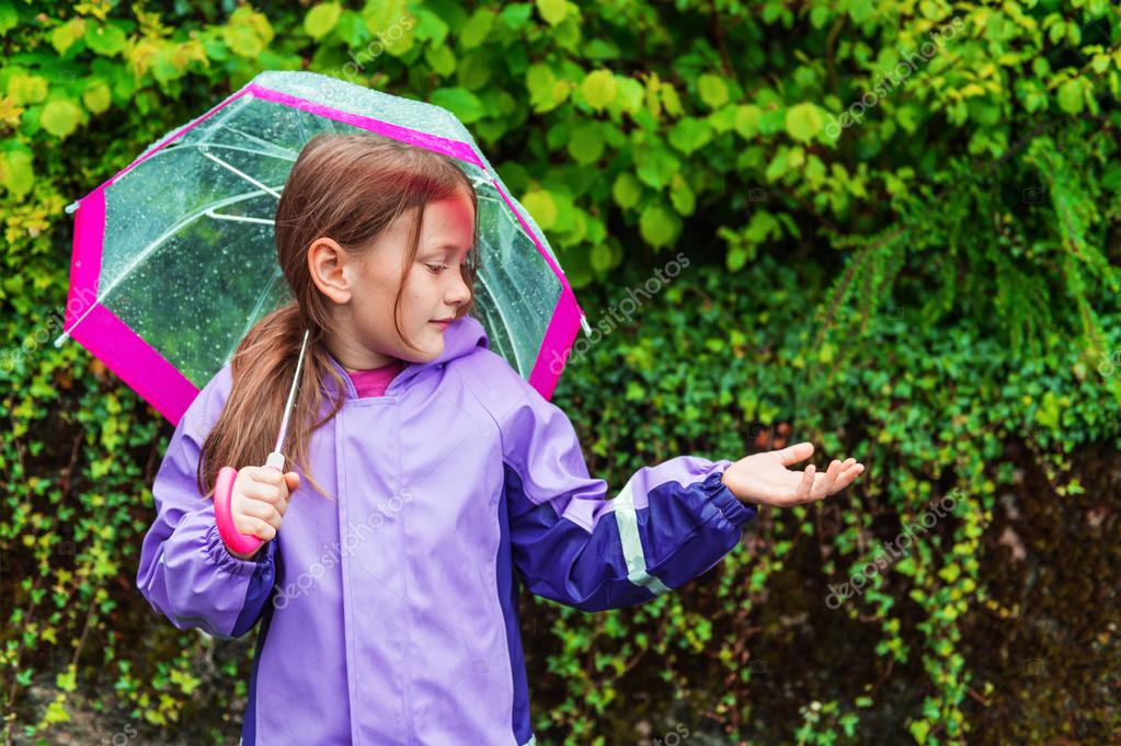 Pretty little girl under the rain, wearing purple rain coat, holding