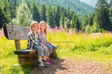 Cute little boy and his sister with backpack hiking in mountains, resting on a bench