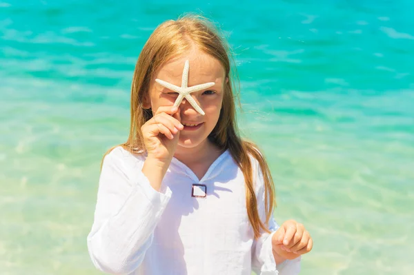 Cute little girl playing with a starfish on the beach on a very hot sunny day — Stock Photo, Image