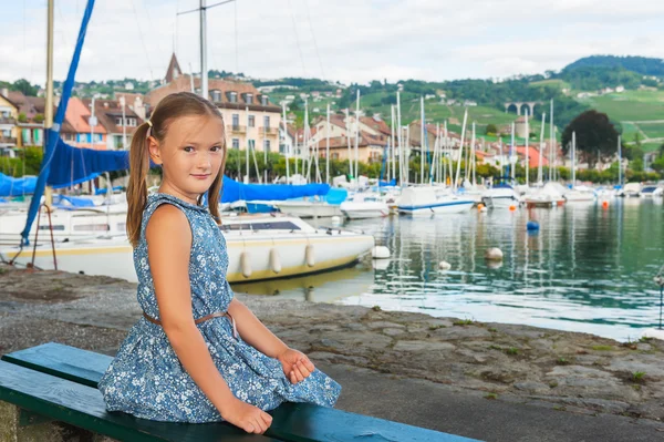 Модный портрет милой маленькой девочки, сидящей на скамейке у озера в синем платье — стоковое фото