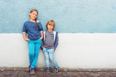 İki çocuk, kız ve açık havada poz, mavi duvara karşı duran bir çocuk,