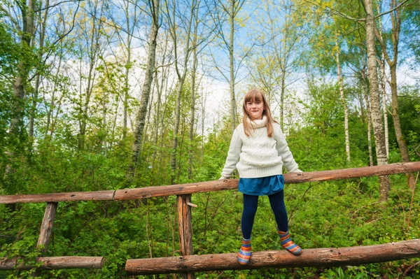 Linda niña senderismo en el bosque de primavera, vistiendo jersey de punto blanco cálido, sentado en la valla — Foto de Stock