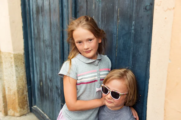 Внешний портрет милых детей, маленькой девочки и ее брата, одетых в серые футболки, стоящих у голубой стены. Туристы Европы — стоковое фото
