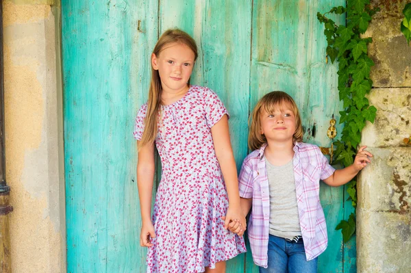 Summer portrait of two cute kids, young girl and her little brother standing against turquoise wooden old door — Stock Photo, Image