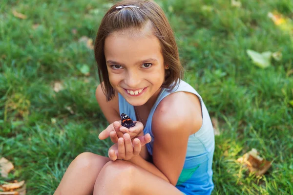 Cute girl playing with butterfly outdoors in the park on a nice summer day — Stock Photo, Image