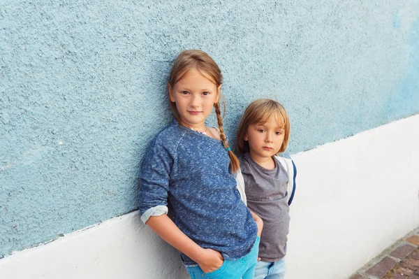 Dois filhos, menina e menino, posando ao ar livre, de pé contra a parede azul — Fotografia de Stock