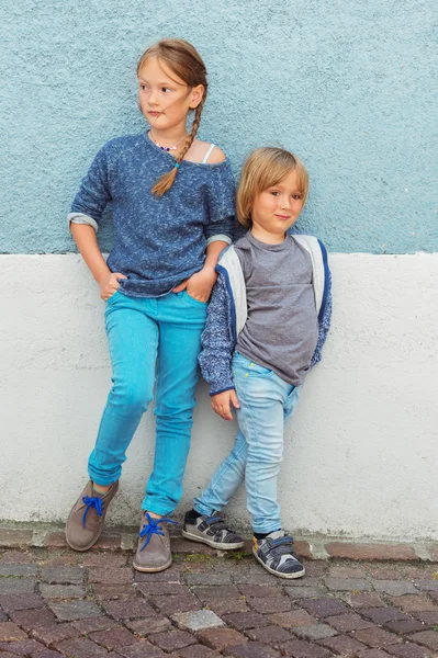 Two kids, girl and little boy, posing outdoors, standing against blue wall — Stock Photo, Image