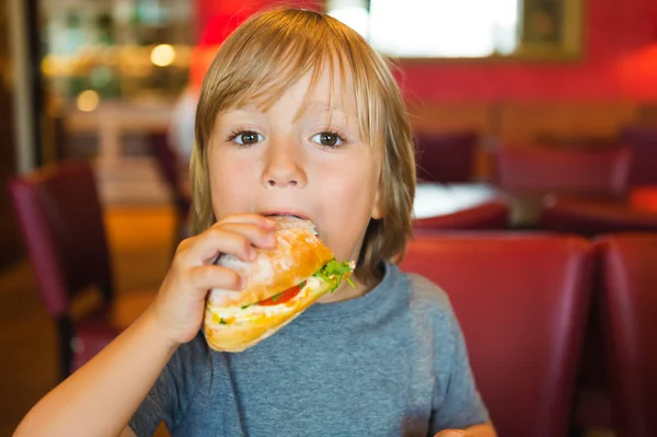 Boy eating big sandwich in cafe — Stock Photo, Image