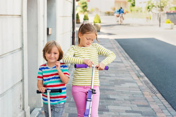 Two cute kids playing outdoors, riding scooters — Stock Photo, Image