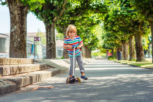 Outdoor portrait of a cute little boy riding scooter in the park — Stock Photo, Image