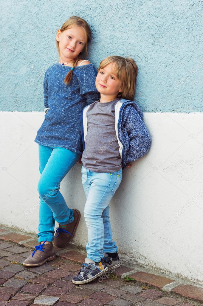 Two kids, girl and little boy, posing outdoors, standing against blue wall