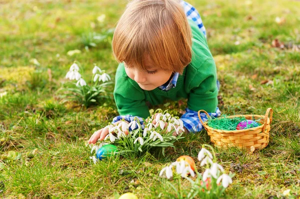 Очаровательный маленький блондин, играющий с яркими пасхальными яйцами в парке, охота за яйцами — стоковое фото