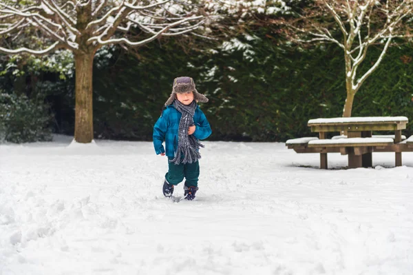 Söt liten pojke spelar i Vinterparken. Kid har roligt utomhus, kör på snö, bär varma blå jacka, mössa och halsduk — Stockfoto