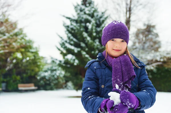 Adorable little girl of 8 years old playing in winter park, wearing warm blue coat, purple set of hat, scarf and gloves — 图库照片