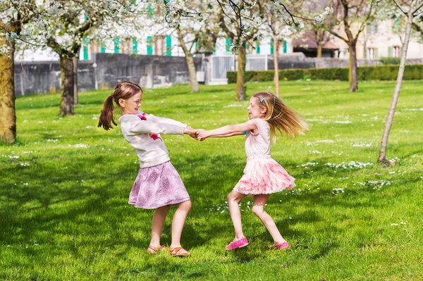 Zwei kleine Mädchen, die an einem sonnigen, warmen Tag im Frühlingsgarten spielen und Röcke tragen — Stockfoto