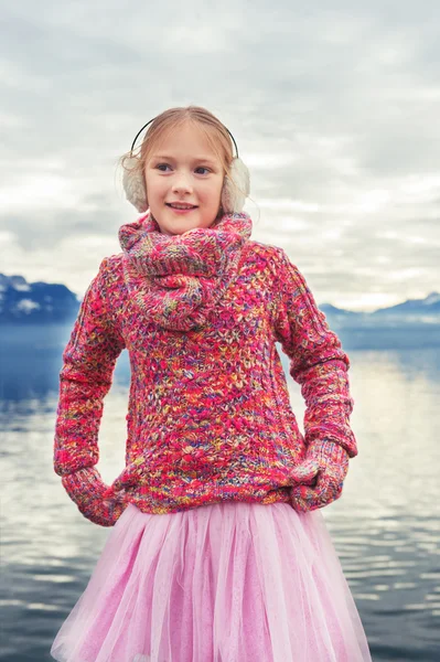 Outdoor close up portrait of adorable little kid girl of 8 years old resting by the lake Geneva on a nice winter day, wearing colorful pink pullover and warm earmuffs — Zdjęcie stockowe