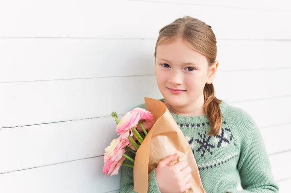 Retrato de adorável menina de 8-9 anos de idade, vestindo pulôver verde quente, segurando flores cor de rosa primavera, de pé contra fundo de madeira branca, conceito de dia da mãe — Fotografia de Stock