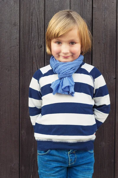 Modeporträt eines entzückenden Jungen vor dunkelbraunem Holzhintergrund, der ein Sweatshirt mit weißen und blauen Streifen trägt — Stockfoto