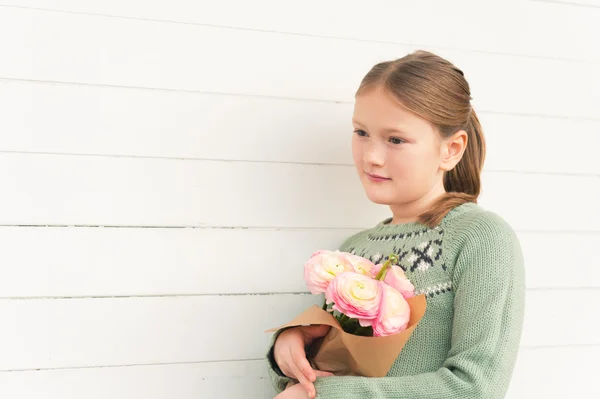 Retrato de adorável menina de 8-9 anos de idade, vestindo pulôver verde quente, segurando flores cor de rosa primavera, de pé contra fundo de madeira branca, conceito de dia da mãe — Fotografia de Stock