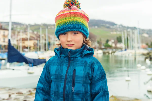Outdoor close up portrait of a cute little boy of 4-5 years old, wearing colorful hat and waterproof blue coat — Stock Fotó