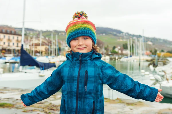 Outdoor close up portrait of a cute little boy of 4-5 years old, wearing colorful hat and waterproof blue coat — Stock Photo, Image