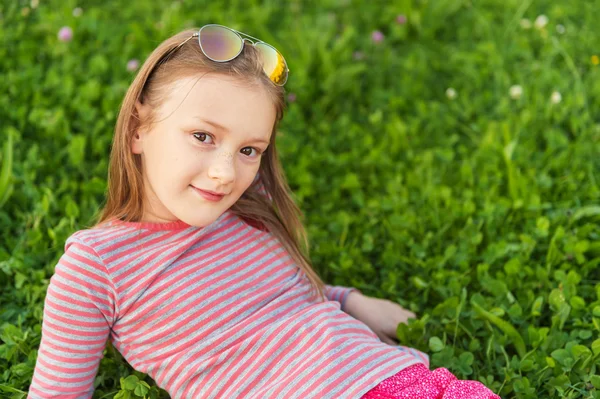 Portrait of a cute little girl of 7 years old in the park, laying on grass, wearing red clothes — Zdjęcie stockowe