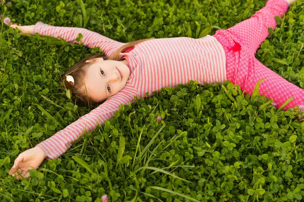 Portrait of a cute little girl of 7 years old in the park, laying on grass, wearing red clothes — ストック写真