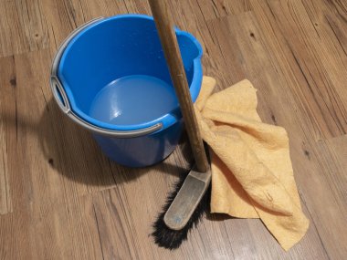 Tahta zeminde temizlik malzemeleri, süpürge, bez, mavi kova, temizlik hazırlığı.
