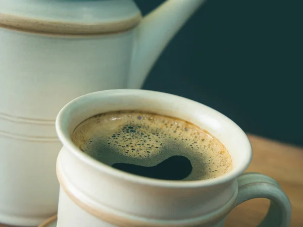 A cup of coffee, in a white cup on wooden table, blurred background, close up, photo