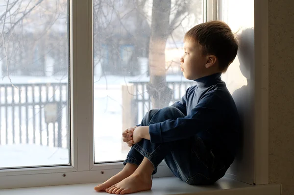 Pojken sitter på fönstret tittar ut — Stockfoto