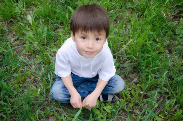 Chłopiec siedzi na trawie poza — Zdjęcie stockowe