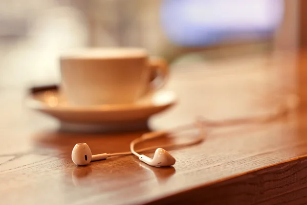 Hoofdtelefoons liggen in de buurt van kopje koffie — Stockfoto