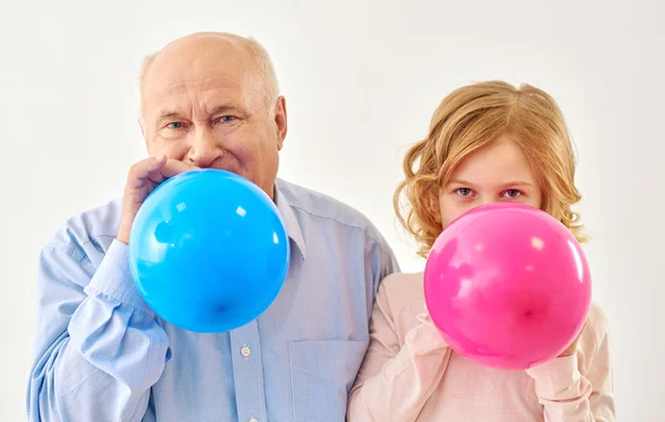 Granddaughter and grandfather inflating balloons in studio — Stock Photo, Image